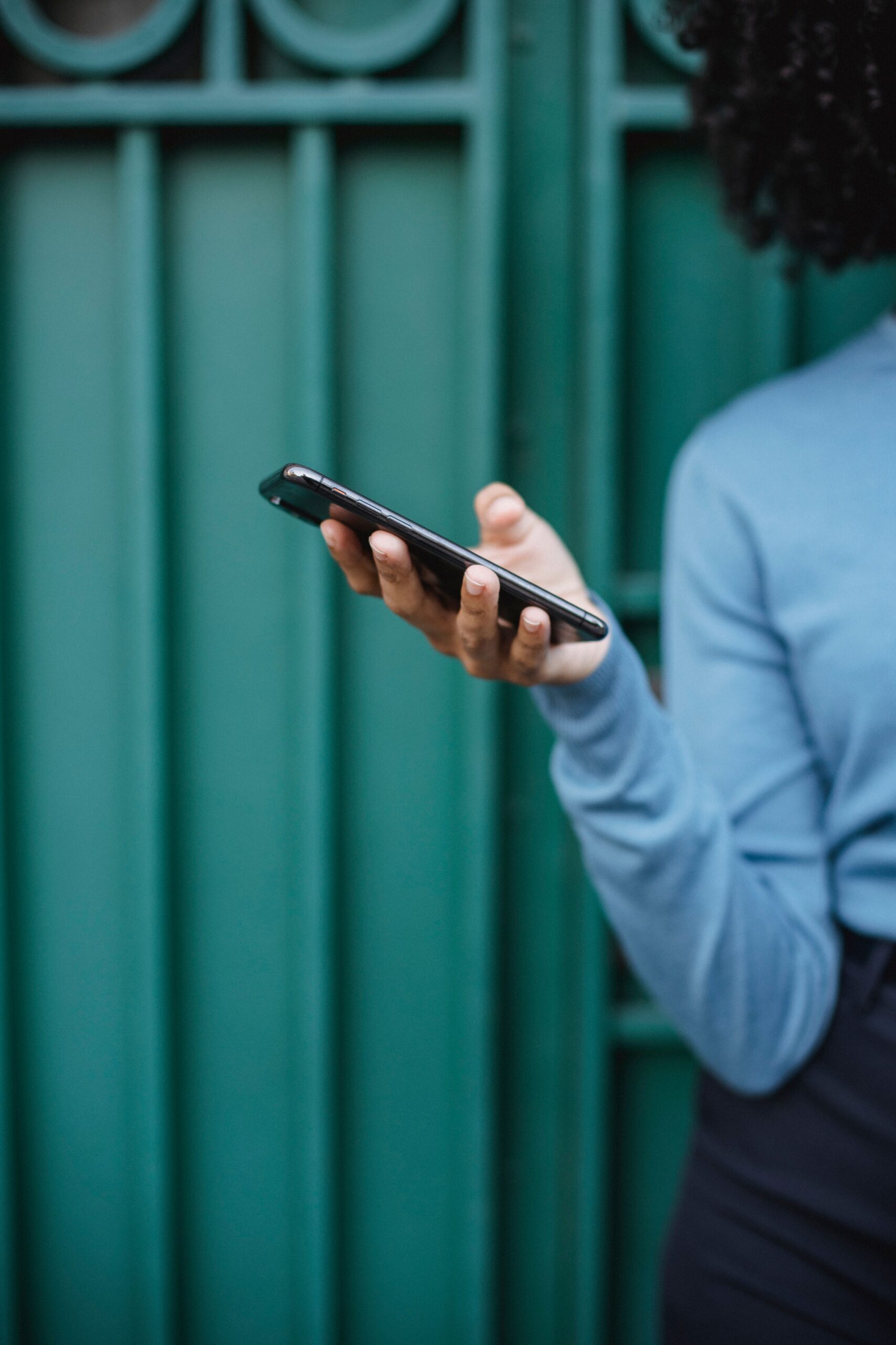 A person in a blue sweater holds a smartphone against a teal urban backdrop. Modern lifestyle concept.